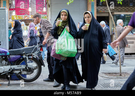 Teheran, Iran - 29. April 2017: Zwei muslimischen Frauen, im schwarzen Tschador gekleidet, mit einem Strohhalm trinken Saft, die ersten Pakete trägt mit Käufen, die se Stockfoto