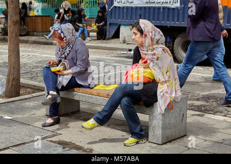 Teheran, Iran - April 29, 2017: Zwei junge Frauen, im hijab gekleidet, sitzen auf einer Parkbank in einer Straße der Stadt. Stockfoto