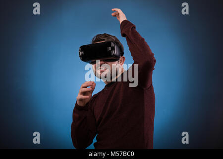 Junge glücklich erleben virtuelle Realität durch ein Headset isoliert auf Blau, Studio gedreht. Stockfoto
