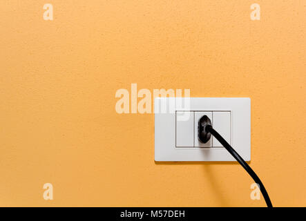 Den schwarzen Stecker in eine Steckdose auf eine orange Wand eingefügt Stockfoto