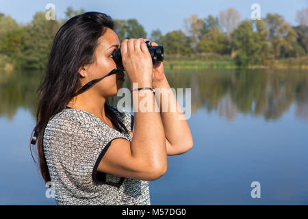 Frau auf der Suche durchs Fernglas am Wasser Stockfoto