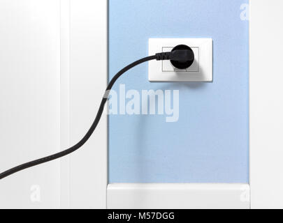 Den schwarzen Stecker in eine Steckdose auf einem hellblauen Wand eingefügt Stockfoto