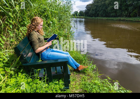 Niederländische Frau liest Buch auf der Werkbank am Wasser Stockfoto