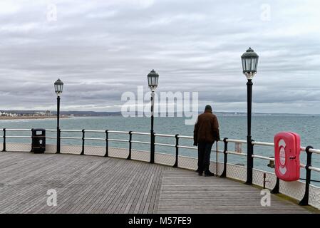 Rückansicht eines einzigen alten Herrn mit Stock, Blick auf das Meer am Ende der Pier Worthing UK an trüben Wintertag zu Stockfoto