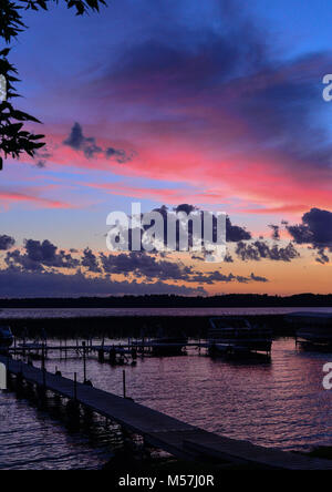 Bild vertikal, lebendige Sonnenuntergang auf See mit Dock und Boote in vibrant Blue, violett, orange und rosa Stockfoto