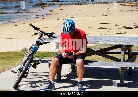 Selbstisolierter Mann, der nach dem Fahrradfahren und dem Überprüfen des Mobiltelefons ruht Stockfoto