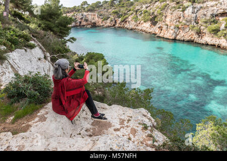 Eine junge brünette Frau mit ergrauendem Haar, einen roten Pullover Schal und ein Foto von der Blick auf Cala Pi auf der Insel Mallorca, Spanien. Stockfoto