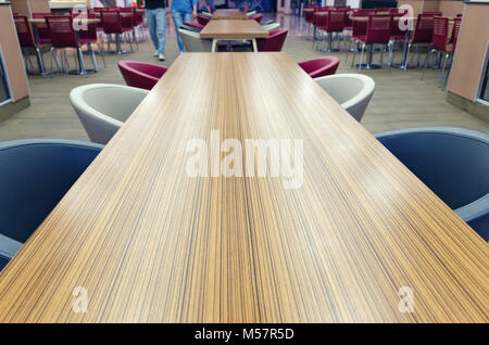 Blick von oben auf die Holz- lange gelb-braunen Tisch mit blauen und weißen Stühlen. Details der Cafe im Einkaufszentrum. Leere Platz für Text. Stockfoto