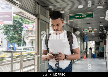 Junger Mann Nachrichten senden oder im Internet surfen auf dem Handy während des Wartens im Innenraum in einem Busbahnhof in Jakarta. Stockfoto
