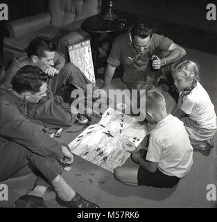 1942, USA, historische, drei Soldaten der United States Army Air Forces (Usaaf) tragen ihren fliegenden Kit in Spielen der neue Vorstand Spiel sitzen, "Air Combat Trainer" mit zwei kleinen Kindern. In Verbindung mit dem Krieg der USA Abteilung produziert, das Spiel war ein Test der Fähigkeit zur Bekämpfung von Fliegen, mit Miniaturen von Kampfflugzeugen und kampfmanöver. Stockfoto