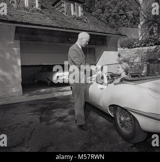 1960er Jahre, USA, historische, Verkäufer die Übergabe an eine Dame am Steuer eines offenen Jaguar Sportwagen, den neuesten Auto Zubehör, in eine Fernsteuerung, die automatisch die Garage öffnet Türen, Los Angeles, Kalifornien. Stockfoto