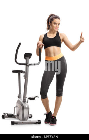 In voller Länge Porträt einer Jugendmädchen lehnend auf einem Cross-trainer Maschine und ein "Daumen hoch" Geste auf weißem Hintergrund Stockfoto