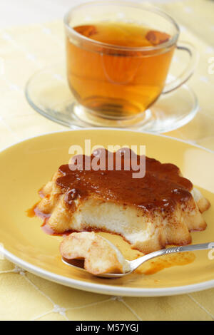 Coconut flan auf gelbem Teller und eine Tasse Tee Stockfoto