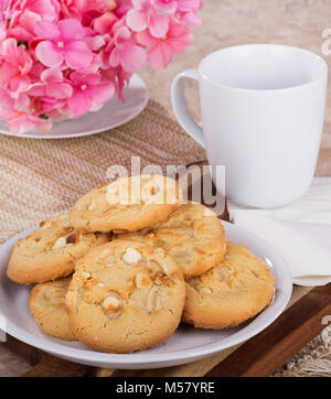 Stapel der Macadamianuss cookies auf einem Teller mit Kaffeetasse und Blumen im Hintergrund Stockfoto