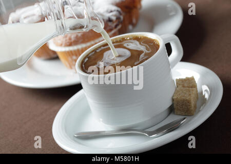 Gießen Milch in Kaffee gegen muffins Stockfoto