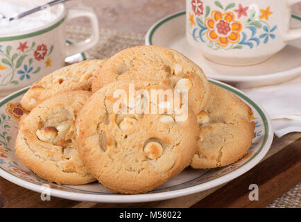 Stapel der Macadamianuss cookies auf einem Teller mit Kaffeetasse und Sugar Bowl im Hintergrund Stockfoto