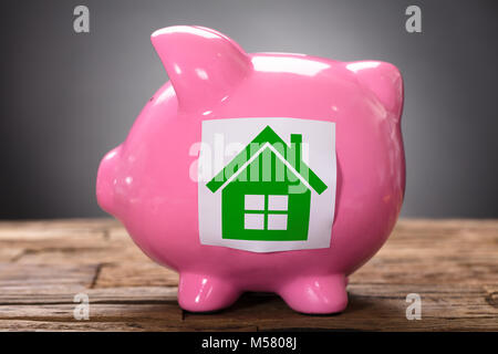 Nahaufnahme des Grünbuchs Haus auf rosa Sparschwein auf Holz Stockfoto