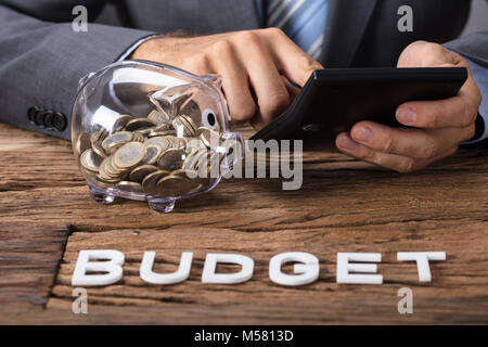 Nahaufnahme der Geschäftsmann mit Taschenrechner durch Sparschwein mit budget Text in Tabelle Stockfoto
