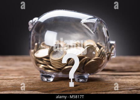 Nahaufnahme von Fragezeichen und Münzen in transparenten Sparschwein auf Tisch Stockfoto