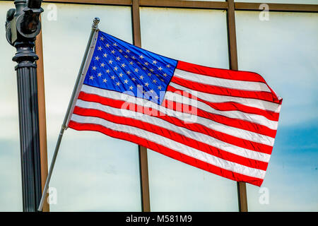 Eine helle, farbenfrohe Amerikanische Flagge zu einem schwarzen angebracht, Bügeleisen pole Wellen in der Brise außerhalb einer Bank Fenster in Littleton, NH, USA. Stockfoto