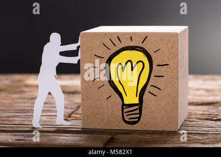 Nahaufnahme von Papier Mann drücken Holzblock mit Glühbirne Symbol auf dem Tisch gegen grauer Hintergrund Stockfoto
