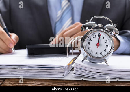 Mittelteil der Geschäftsmann Berechnung Rechnung mit Wecker auf Dokumente bei Tisch Stockfoto