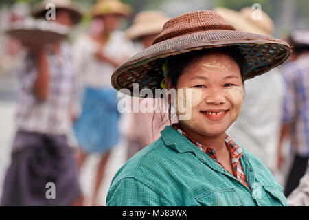 Eine Frau lächelt, als sie hilft, eine Straße in Kalay, einer Stadt in Myanmar. Die Frau trägt thanaka, ein kosmetischer einfügen, auf ihrem Gesicht. Stockfoto