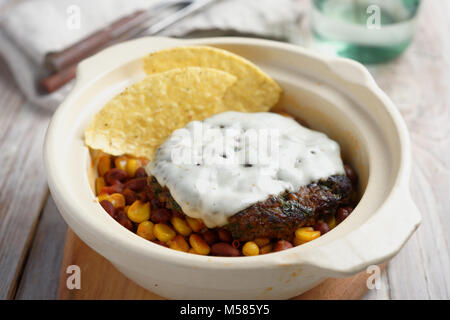 Beef Burger mit Käse, Mais und Bohnen garnieren schmelzen, und Mais Chips in einem rustikalen Pot Stockfoto