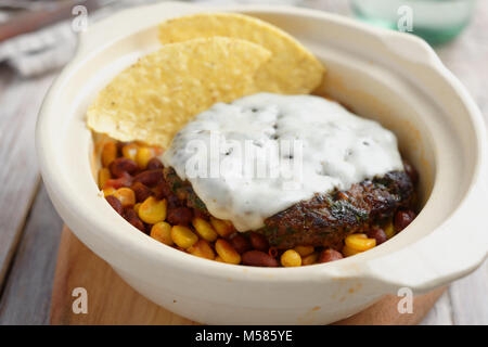 Beef Burger mit Käse, Mais und Bohnen garnieren schmelzen, und Mais Chips in einem rustikalen Pot Stockfoto