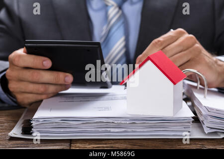 Mittelteil der Geschäftsmann Berechnung Rechnung mit Modell home auf Dokumente bei Tisch Stockfoto