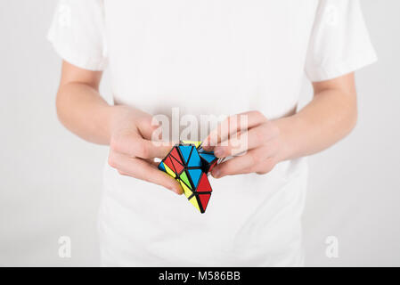 Teenager Geschwindigkeit Lösung 4-seitig Pyraminx Pyramide Puzzle im weißen T-Shirt mit weissem Hintergrund Stockfoto