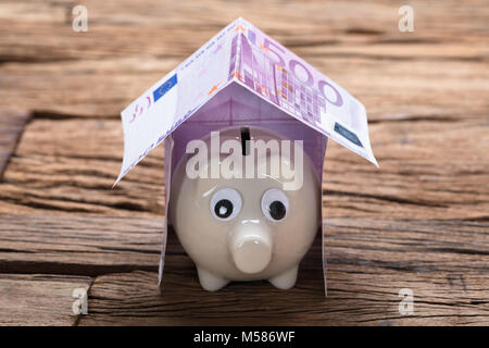 Nahaufnahme von sparschwein im Modell Home von Euro-banknoten auf hölzernen Tisch Stockfoto