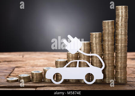 Nahaufnahme des elektrischen Auto gegen gestapelte Münzen auf Holztisch auf schwarzem Hintergrund Stockfoto