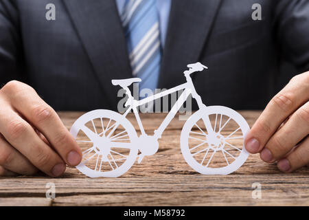 Mittelteil der Geschäftsmann holding Papier Fahrrad an den hölzernen Tisch Stockfoto