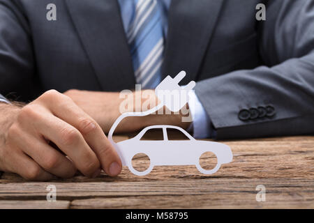 Mittelteil der Geschäftsmann holding Papier Elektroauto an den hölzernen Tisch Stockfoto