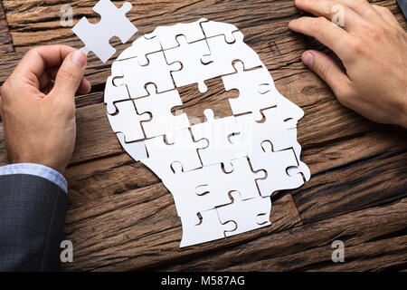 Zugeschnittenes Bild des Geschäftsmannes holding Papier Puzzle Stück, während sie den Kopf auf hölzernen Tisch Stockfoto