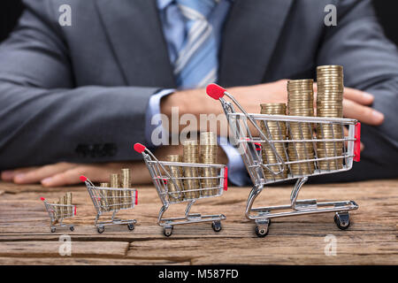 Mittelteil der Geschäftsmann an den hölzernen Tisch sitzen mit Münzen in Shopping Carts Stockfoto