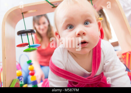 Nahaufnahme Porträt einer niedlichen Baby Mädchen mit blauen Augen und einem intelligenten Gesichtsausdruck, während sie auf dem Boden mit ihrer Mutter zu Hause Stockfoto