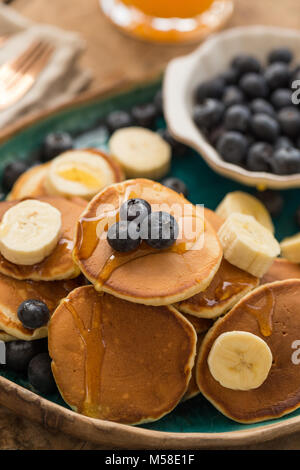 Closeup Schuß von Pfannkuchen in einem türkis Keramikplatte mit Blaubeeren und Banane. Vertikale Komposition. Stockfoto