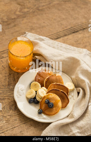 Pfannkuchen mit Heidelbeeren, Bananen und Orangensaft über rustikal Hintergrund. Stockfoto