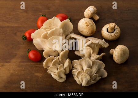 Gemüse: Blick von oben auf die Auster und Champignons mit roten Baby Tomaten isoliert auf braunem Holz- Hintergrund Stockfoto