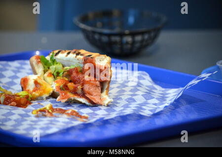 Detail einer unordentlichen Hot dog Brötchen mit Gewürzen auf einem blauen Fach in einem Fast-Food-Restaurant Stockfoto