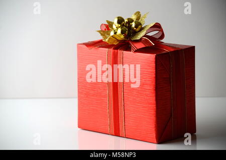 Stilvolle Geschenkverpackung in einem hellen Rot Geschenkpapier mit einem goldenen Band und Bogen auf einer festen grauen Hintergrund mit Kopie Raum gewickelt. Stockfoto