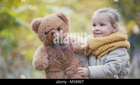 Kleine blonde Mädchen spielt mit Teddybär im Herbst Park Stockfoto