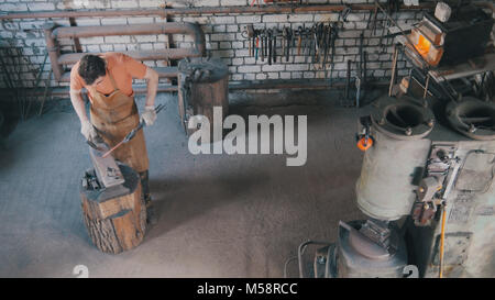 Bart mann Schmiede in der Schmiede macht Metall Werkzeuge auf Eisen Amboss mit Hammer, Ansicht von oben Stockfoto