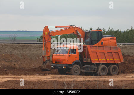 Schwere Hydraulikbagger laden Muldenkipper im Straßenbau zwischen Feldern Stockfoto