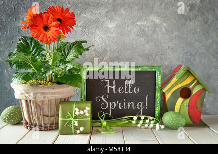 Ostern Dekorationen auf grauem Beton Hintergrund. Tafel mit Frühling Dekorationen: Orange Gerbera, Maiglöckchen, Vogelhaus und malte Ostern Stockfoto