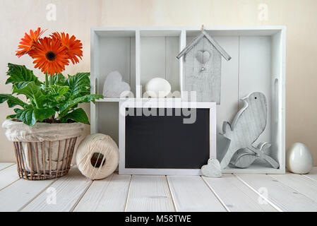 Frühling Hintergrund mit Frühling Dekorationen. Vitrine mit verschiedenen Objekten und Orange Gerbera Flower Pot. Spacefor ihr Text auf einem blackboar Stockfoto