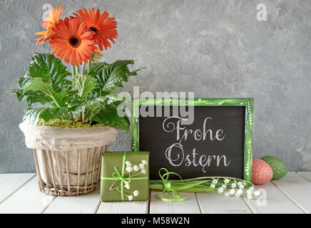 Frühling Blumen, Ostern Dekorationen und eine Tafel mit weißer Tisch. Text "Frohe Ostern", das bedeutet "Frohe Ostern!" im Englischen auf einer Tafel. Stockfoto