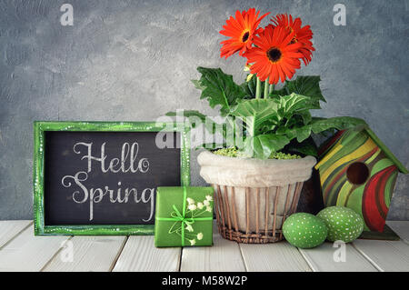 Ostern Dekorationen auf grauem Beton Hintergrund. Tafel mit Frühling Dekorationen: Orange Gerbera, Maiglöckchen, Vogelhaus und malte Ostern Stockfoto